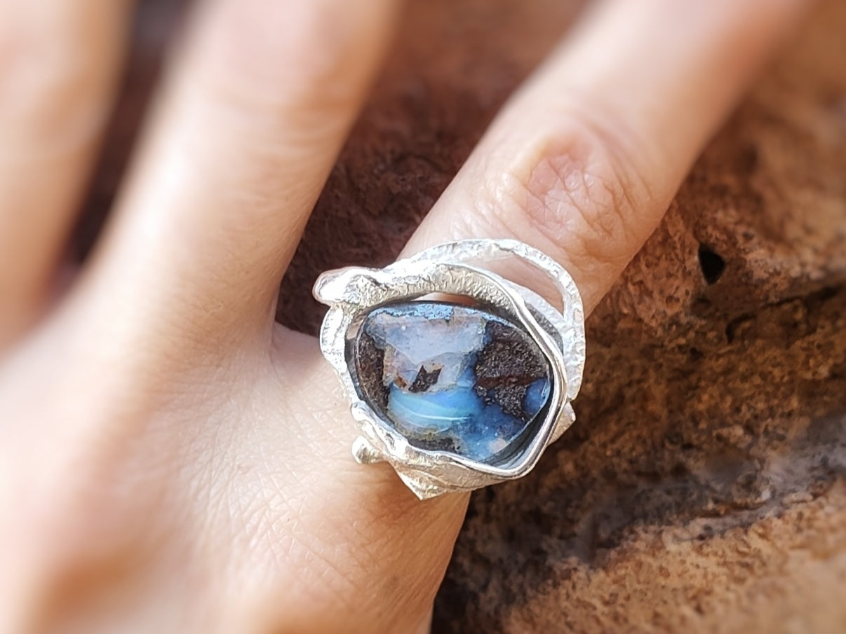 Primer plano del anillo plateado con la piedra ópalo Boulder es en un dedo.
