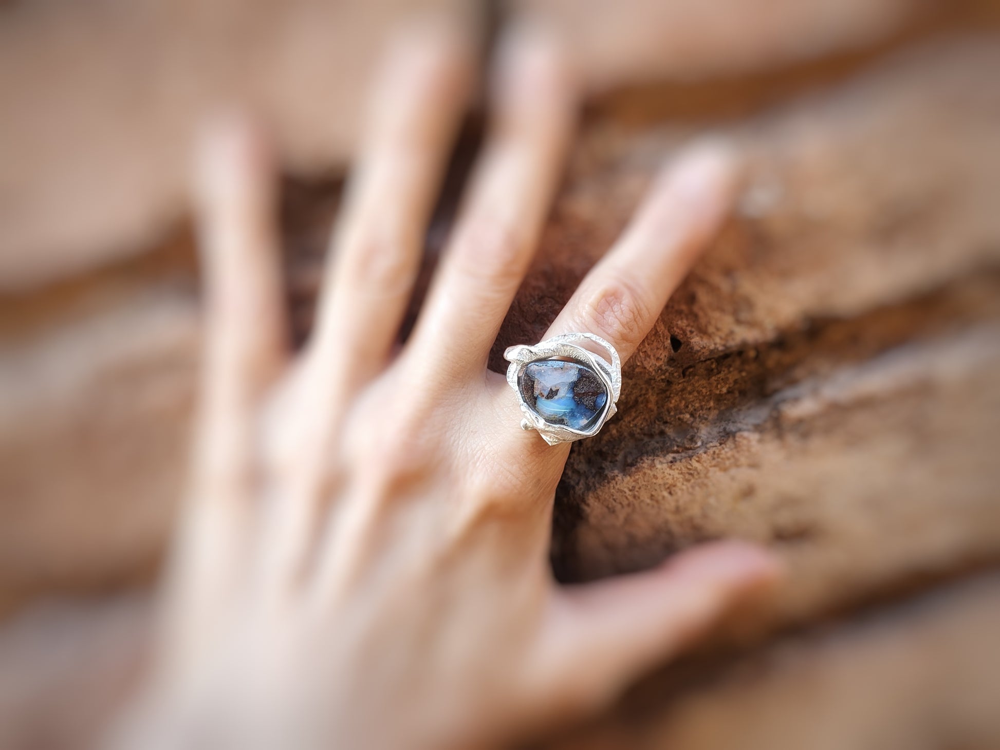 Primer plano del anillo plateado con la piedra ópalo Boulder es en un dedo.