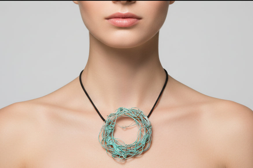 Colgante artesanal de cobre esmaltado en tonos turquesa, con forma orgánica y cordón negro.