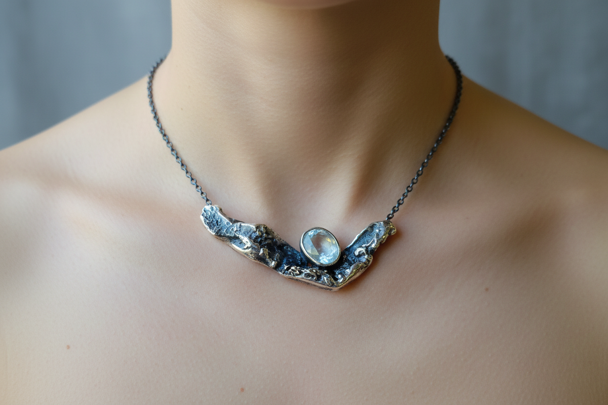 Colgante artesanal de plata 925 con aguamarina natural, llevado al cuello; la pieza muestra un diseño orgánico y texturizado en tonos oscuros y metálicos, con la piedra en el centro, fotografiado en un primer plano sobre la piel