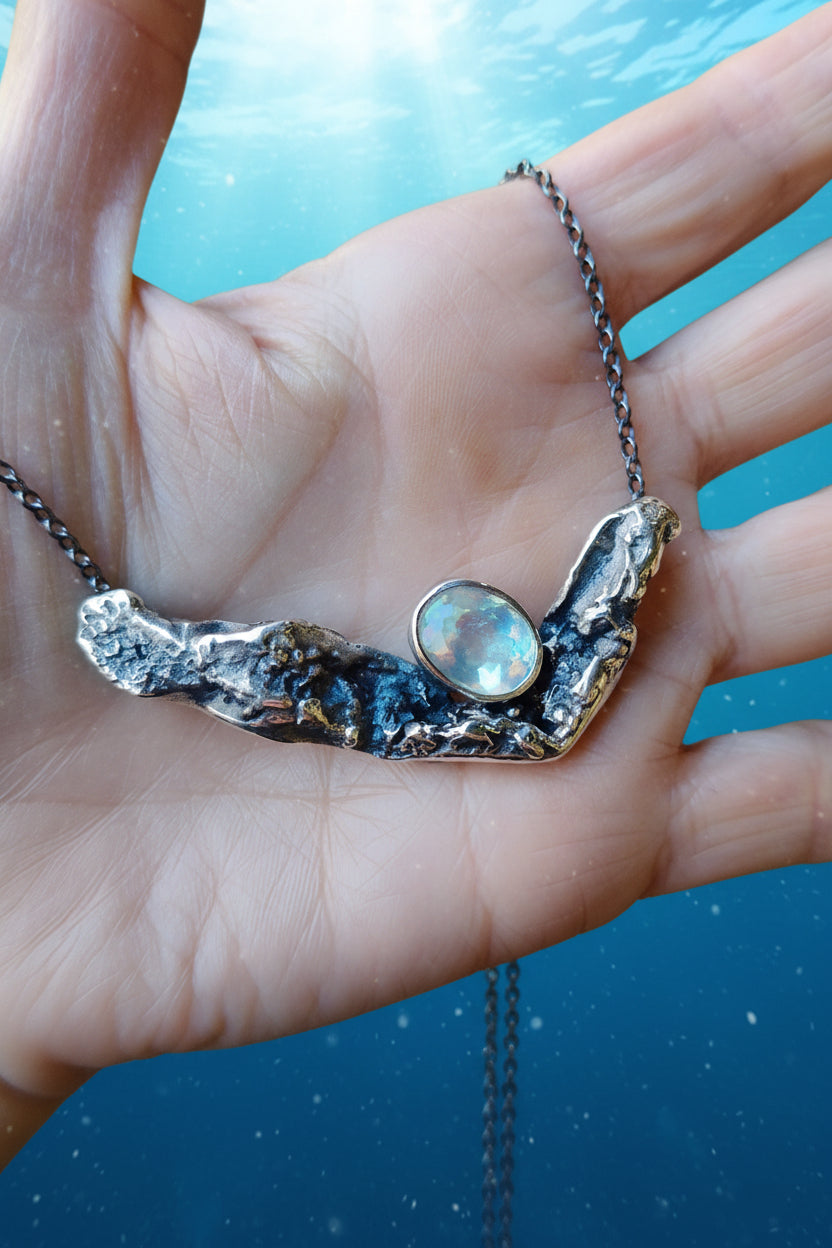 Colgante artesanal de plata 925 con aguamarina natural, sostenido en la mano sobre un fondo azul que representa el mar con pequeños destellos de luz